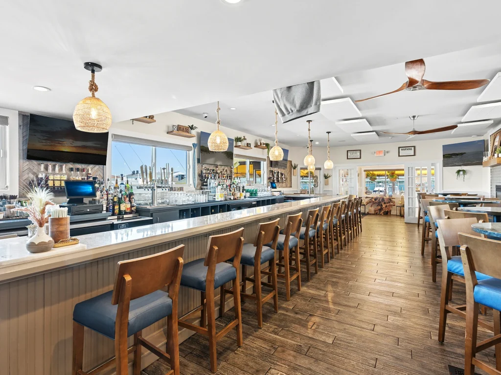 Modern bar interior with wooden stools, marble countertop, and wicker lights.
