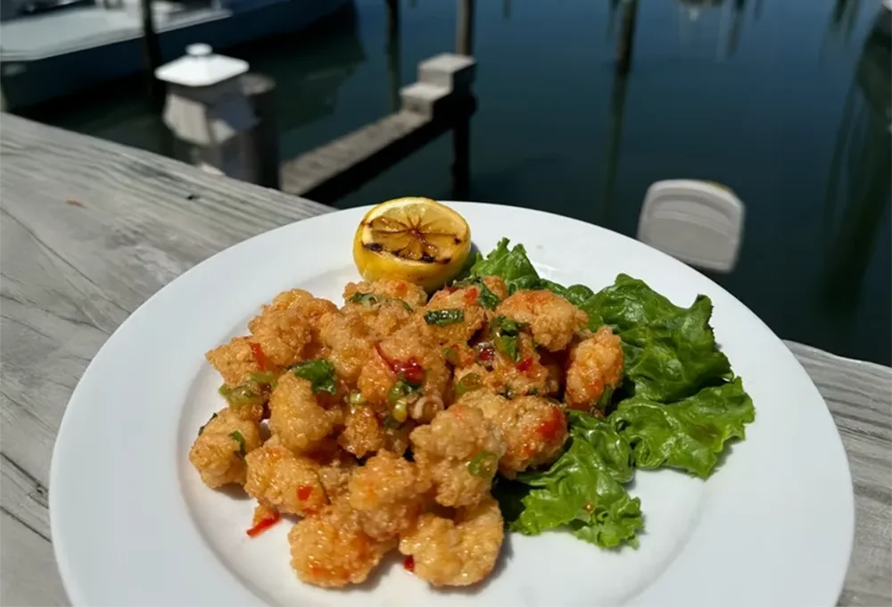 A plate of fried shrimp with lettuce and grilled lemon by a waterfront marina.