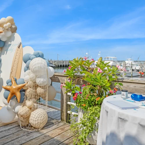 Beach-themed event setup on a pier with balloons, starfish decor, and a view of a marina.