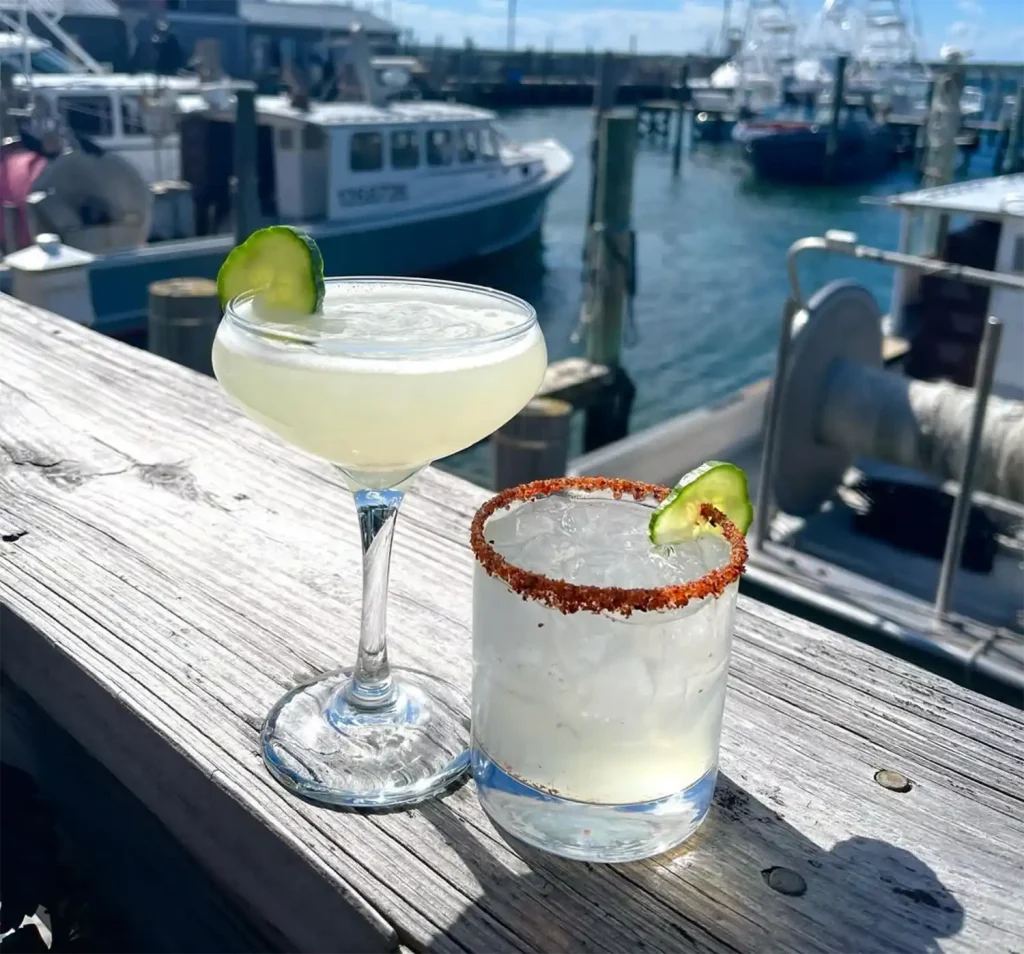 Two cocktails on a wooden pier with boats in the background.