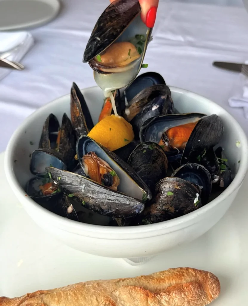 Bowl of mussels with lemon wedge and a hand squeezing mussel juice.