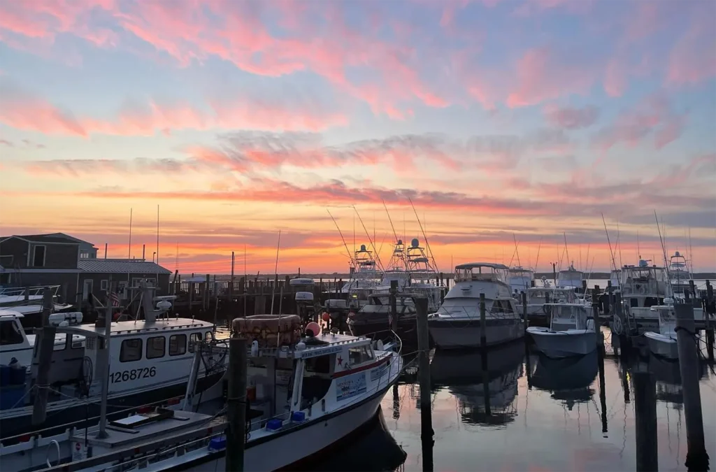 Marina at sunset with boats and colorful sky.